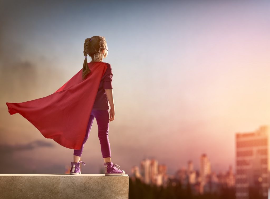 Little girl wearing a red cape being a superhero in her imagination