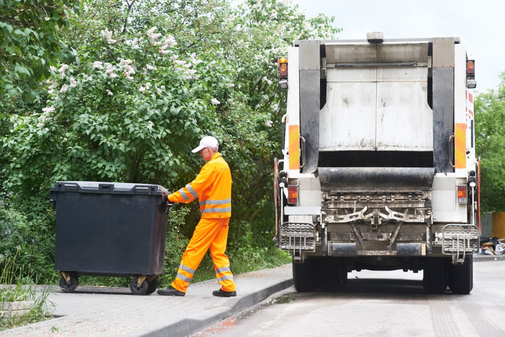 Worker of municipal recycling garbage collector truck loading waste and trash bin